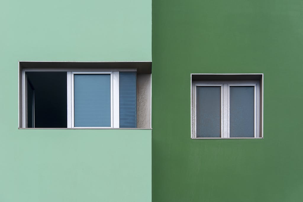 Minimalist facade showcasing two windows on contrasting green walls.